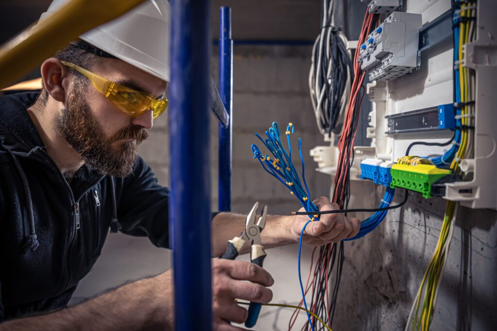 A male electrician works in a switchboard with an electrical connecting cable.