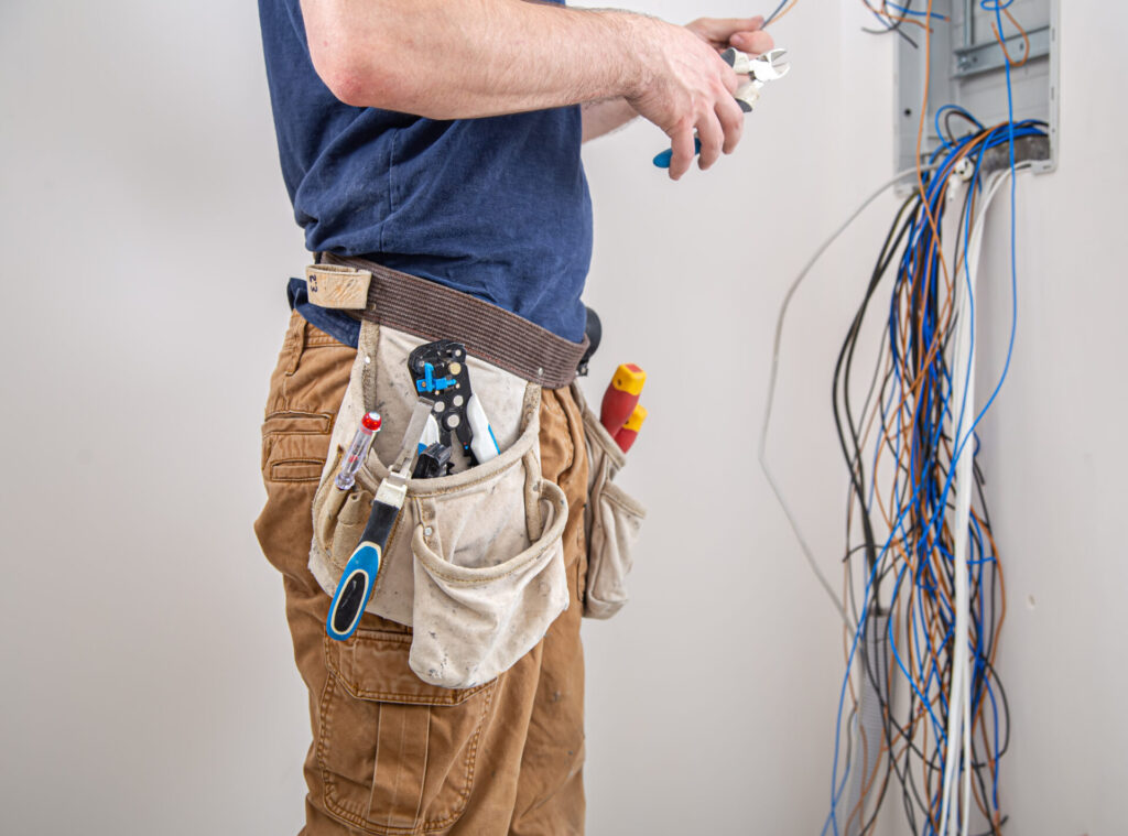Electrician builder examines the cable connection in the electrical line in switchboard indoor.