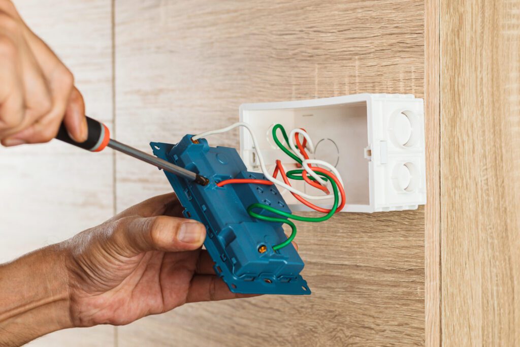 Hand of an electrician is using a screwdriver to attach the wires to the socket.