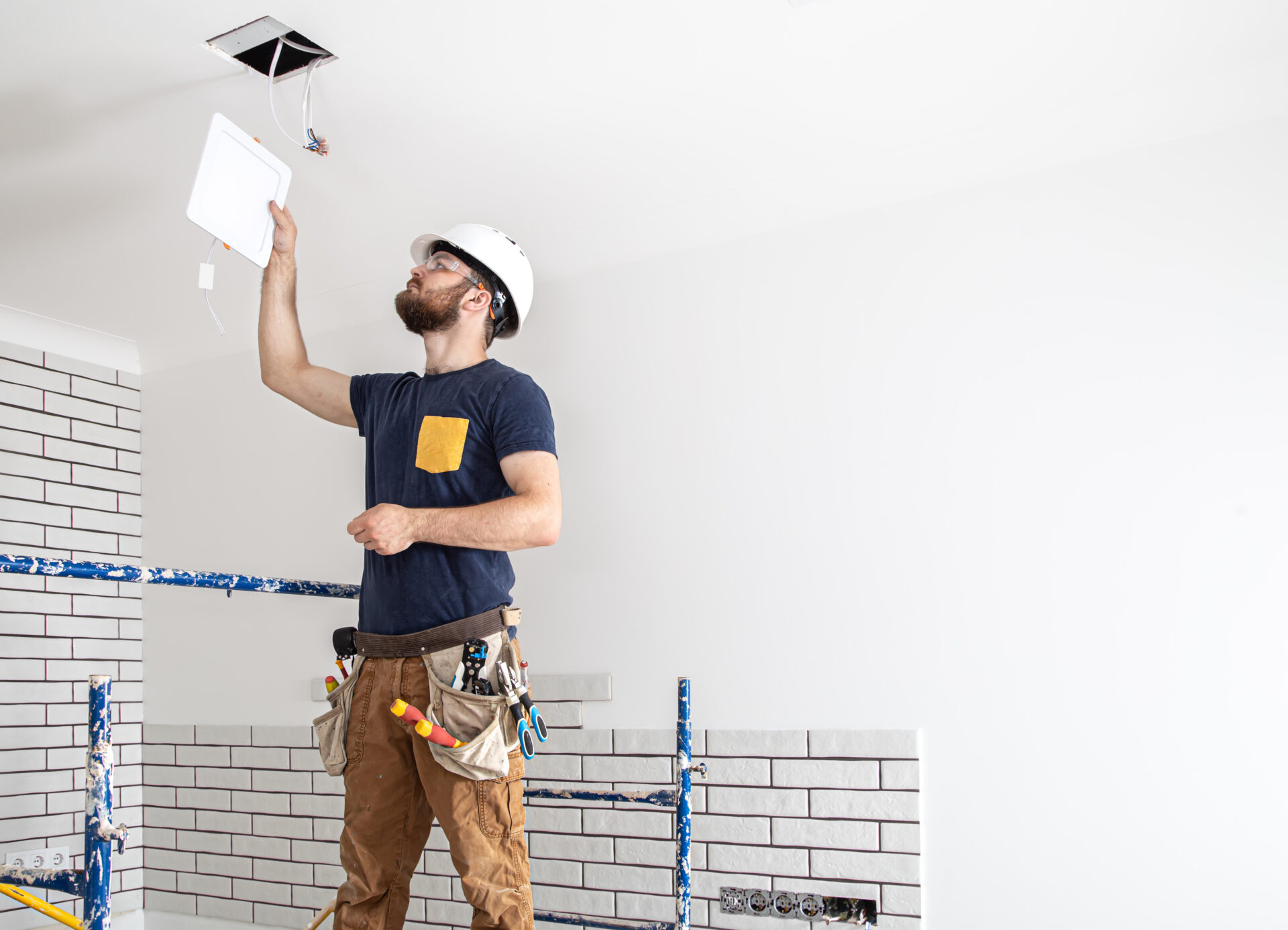 Electrician builder worker in a white helmet, installation of lamps at height copy space.