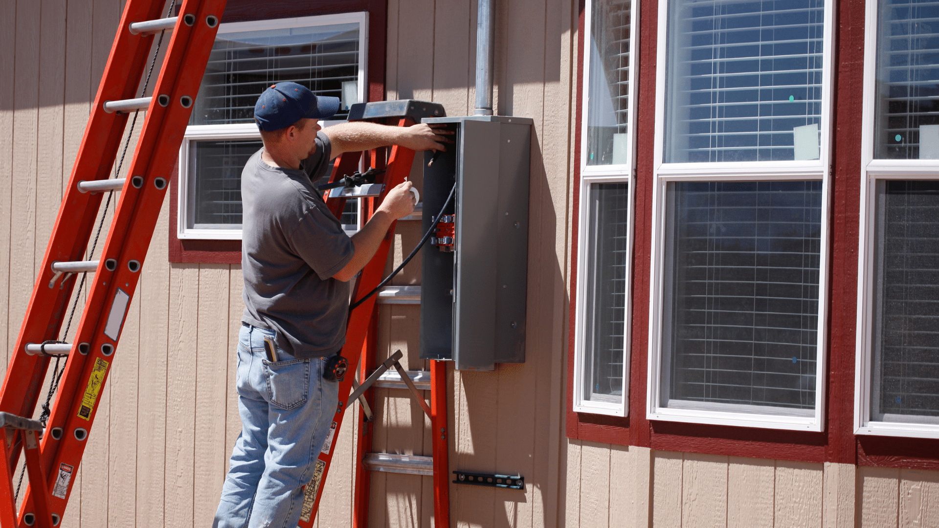 Electrician working on an electrical panel upgrade outside a home, with a red ladder nearby, highlighting electrical service improvements in Newton, IA.