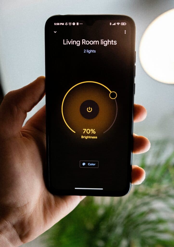 Smartphone displaying smart home lighting control interface for living room, showing brightness level at 70% and options for color adjustment.