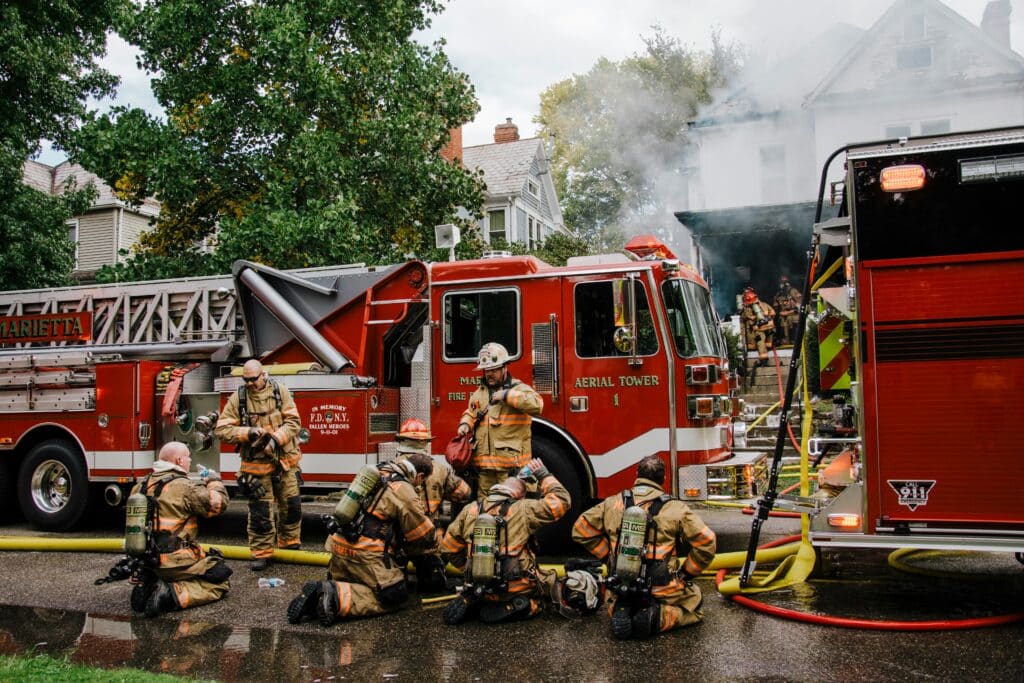 Firefighters in protective gear responding to a house fire, with a fire truck and smoke visible, highlighting the importance of electrical safety and emergency response.