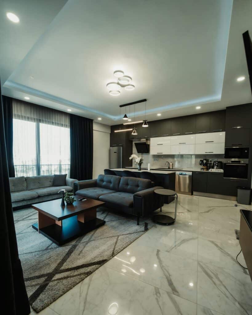 Modern living room featuring recessed lighting, sleek gray sofa, coffee table, and open kitchen area with appliances, emphasizing design and potential noise issues from fixtures.