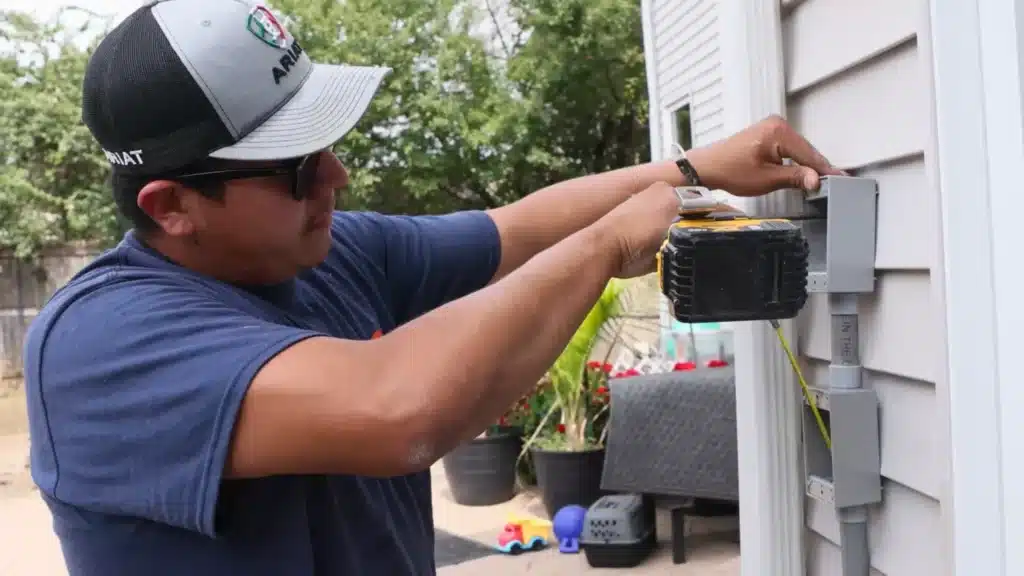 Electrician using a power drill to install electrical conduit on an exterior wall, demonstrating hands-on electrical repair work in a residential setting.