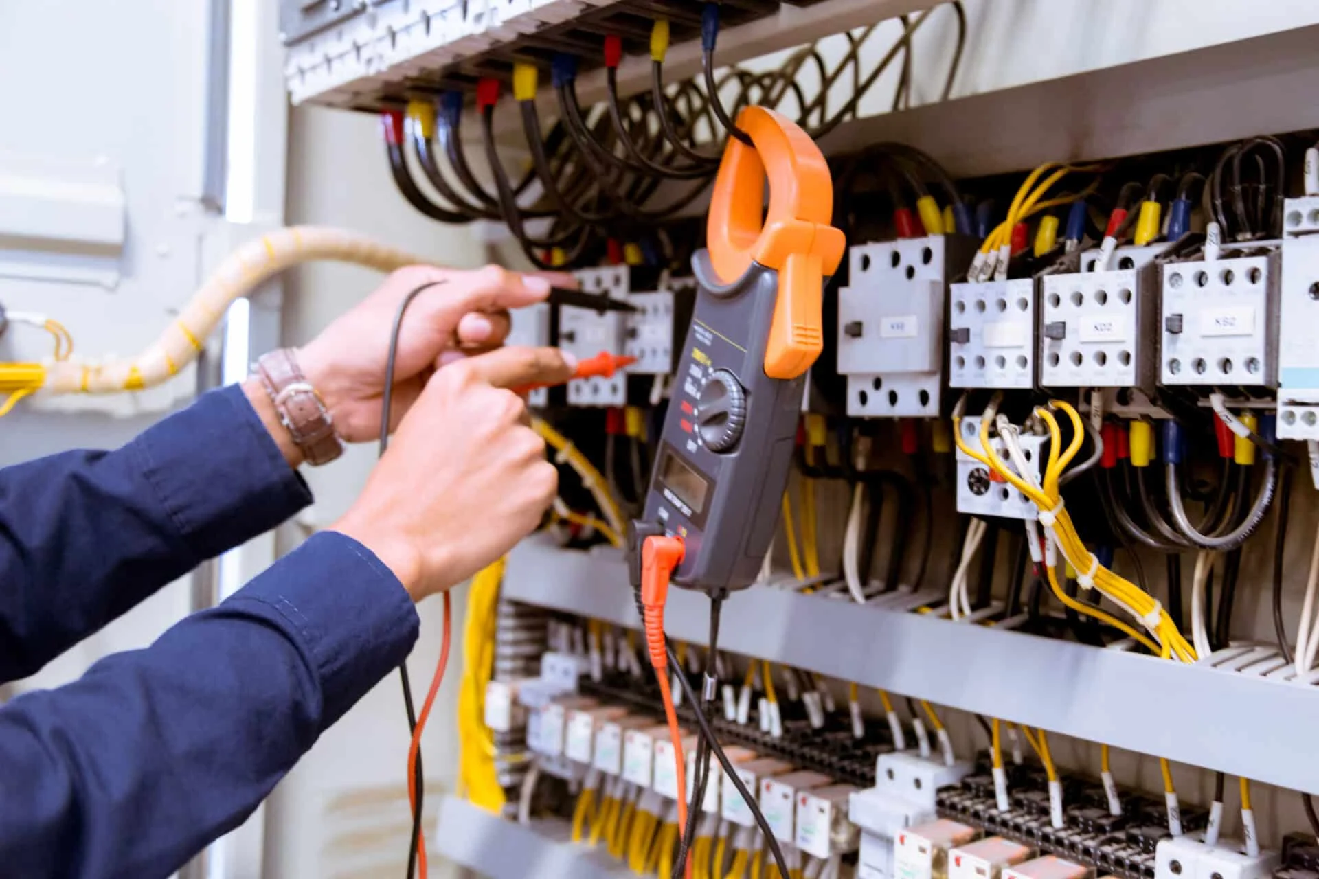 Electrician using multimeter to test electrical system components in a residential setting, emphasizing the importance of electrical maintenance and safety in homes.
